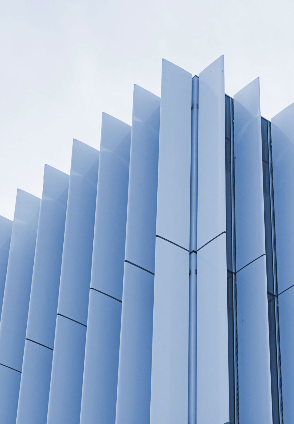 Photo of the corner of a light blue and black skyscraper building taken from below whose facade resembles an accordion.